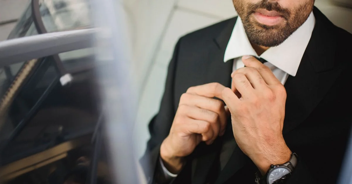 Homme élégant en costume noir ajustant sa cravate, dégageant confiance et style.