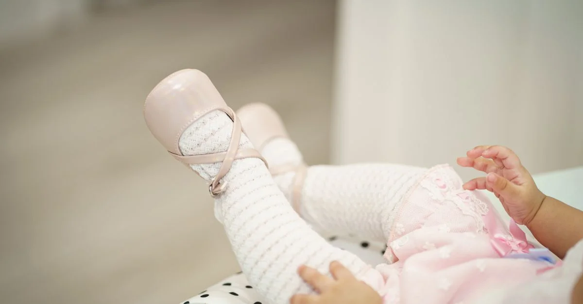 De adorables petits pieds de bébé portant des chaussons de ballet roses et des chaussettes blanches, allongés à l'intérieur.