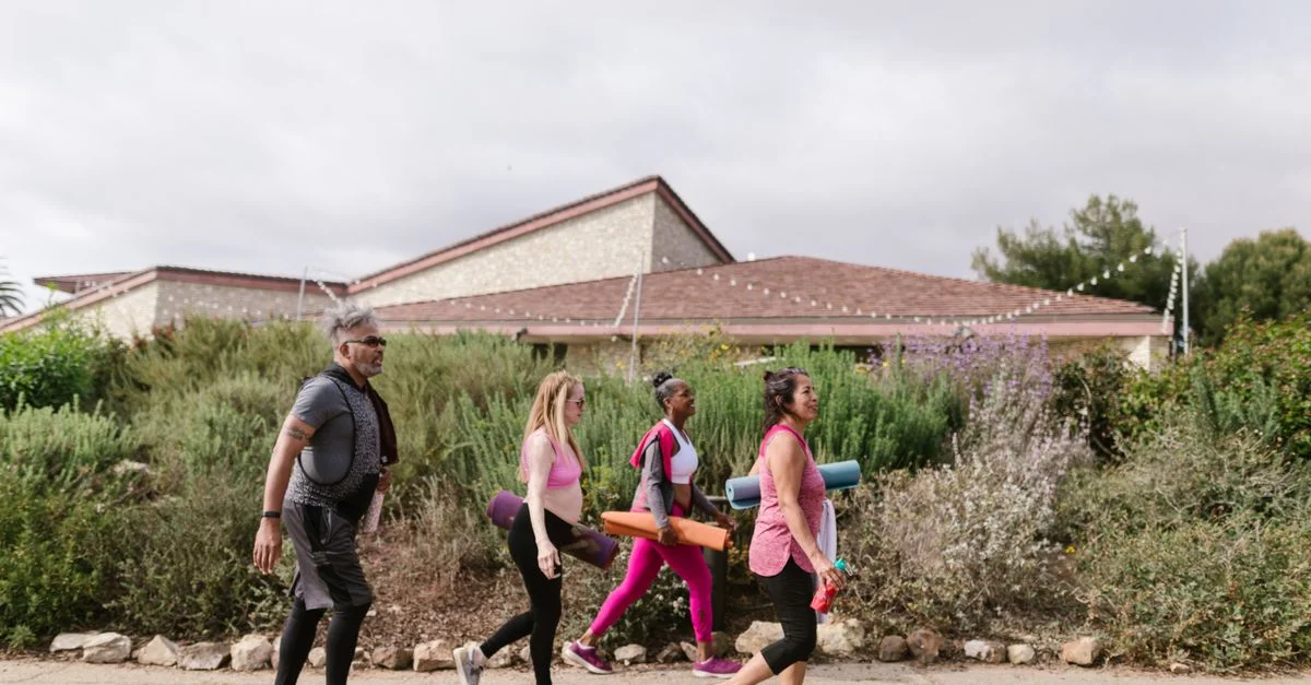 Un groupe d'adultes portant des tapis de yoga marchant à l'extérieur, promouvant la santé et un mode de vie actif.