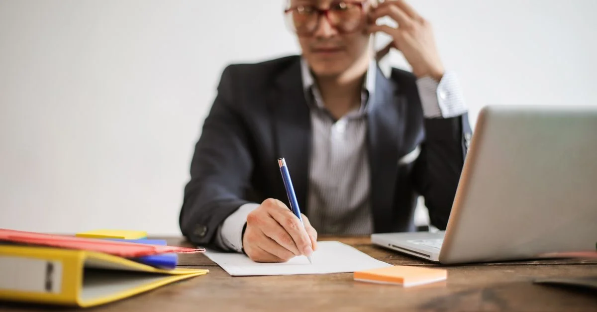 Un homme d'affaires parlant au téléphone tout en prenant des notes et utilisant un ordinateur portable à son bureau.