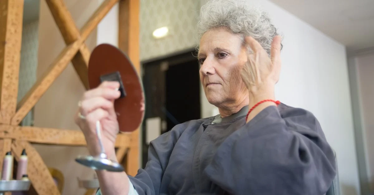 Femme âgée examinant sa nouvelle coiffure dans un salon tout en tenant un miroir à main.