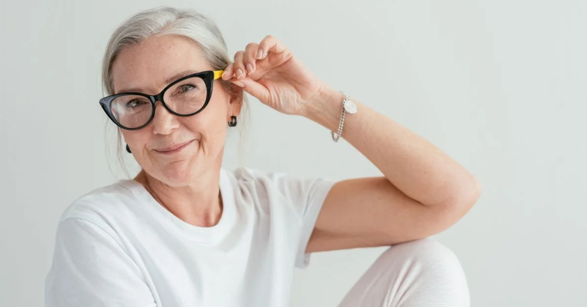 Une femme senior heureuse portant des lunettes élégantes pose à l'intérieur avec un sourire chaleureux.