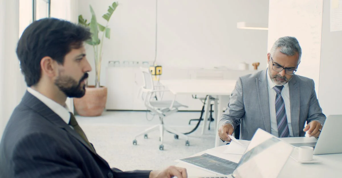 Deux hommes d'affaires en costumes formels travaillant sur des ordinateurs portables dans un bureau moderne.