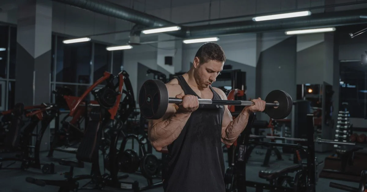 Homme musclé soulevant intensément une barre dans un environnement de gym bien équipé.