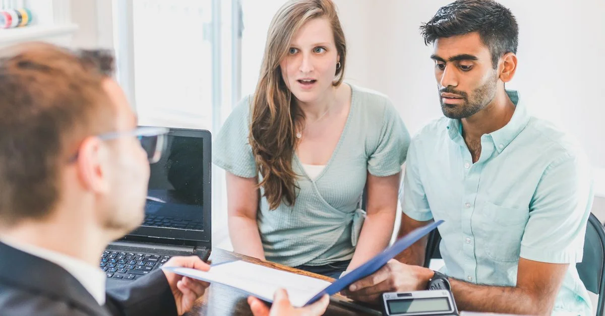 Un jeune couple discute des options d'achat immobilier avec un agent immobilier à l'intérieur.
