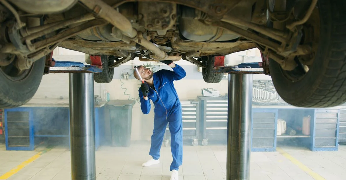 Un mécanicien en uniforme bleu inspecte une voiture levée dans un atelier de garage.