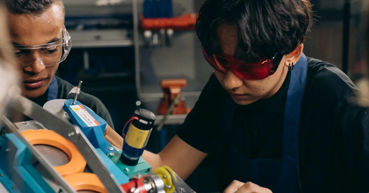 Deux jeunes ingénieurs se concentrant sur un travail de précision dans un atelier technique, portant des lunettes de sécurité.