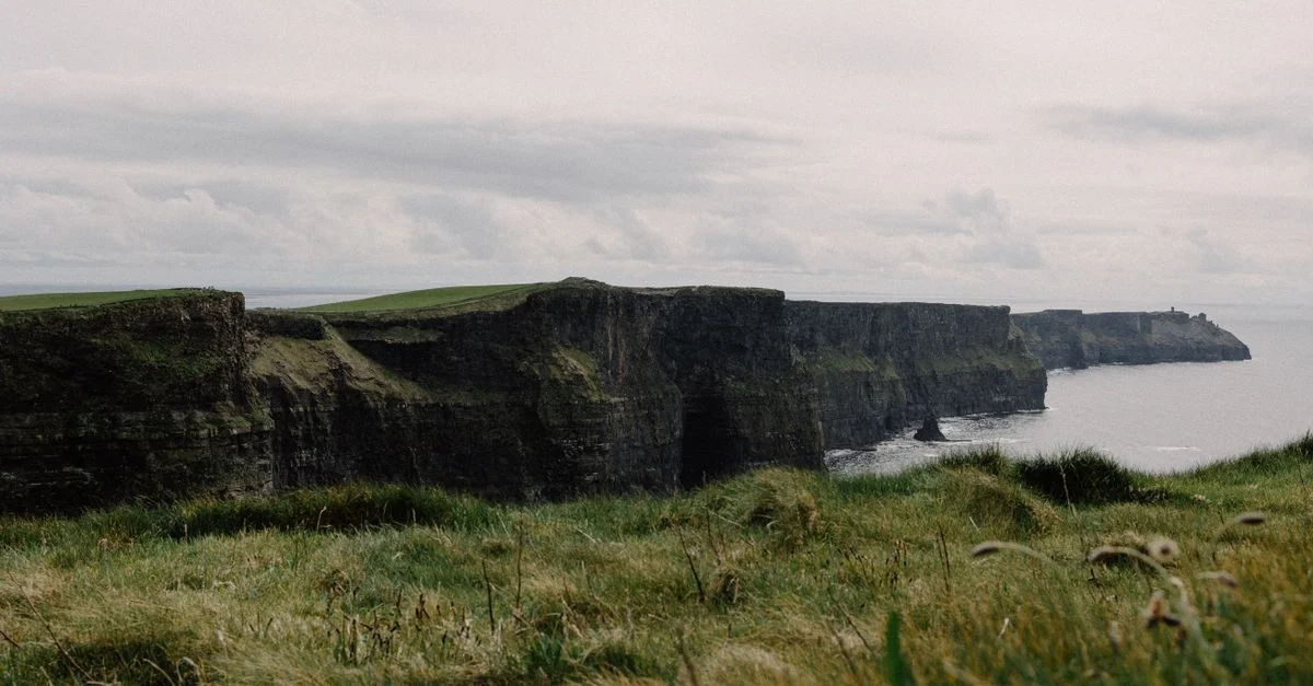Une vue spectaculaire des falaises de Moher avec une herbe luxuriante et un ciel nuageux.