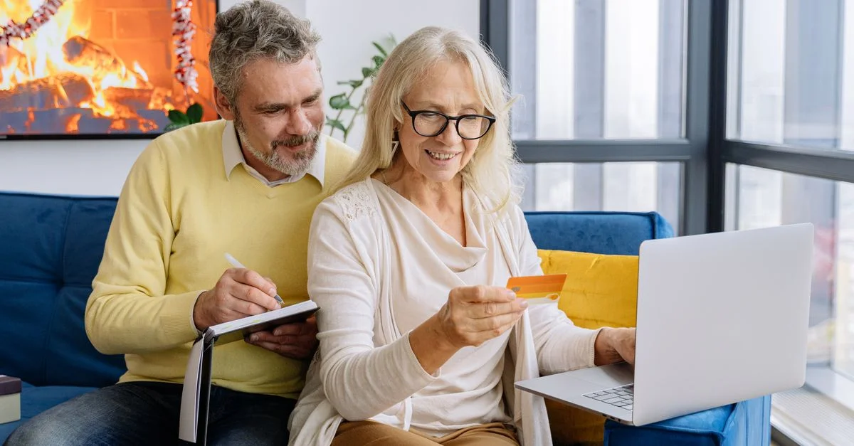 Un couple senior faisant des achats en ligne ensemble avec un ordinateur portable à l'intérieur, adoptant la technologie.
