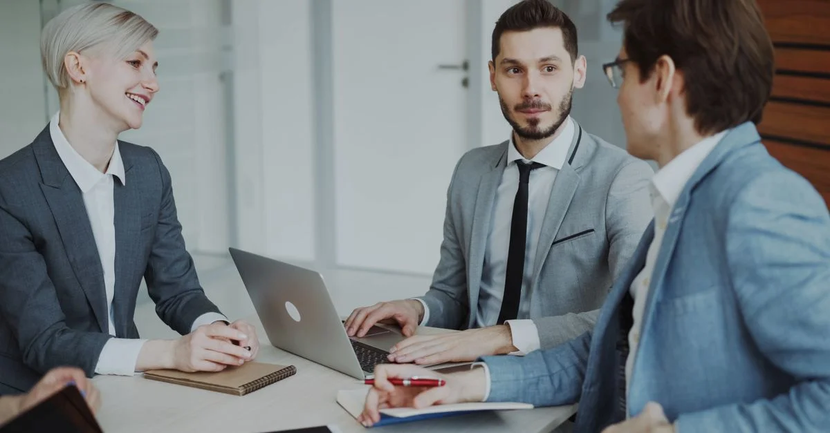 Professionnels en affaires lors d'une réunion avec des ordinateurs portables et des carnets, discutant de stratégie.