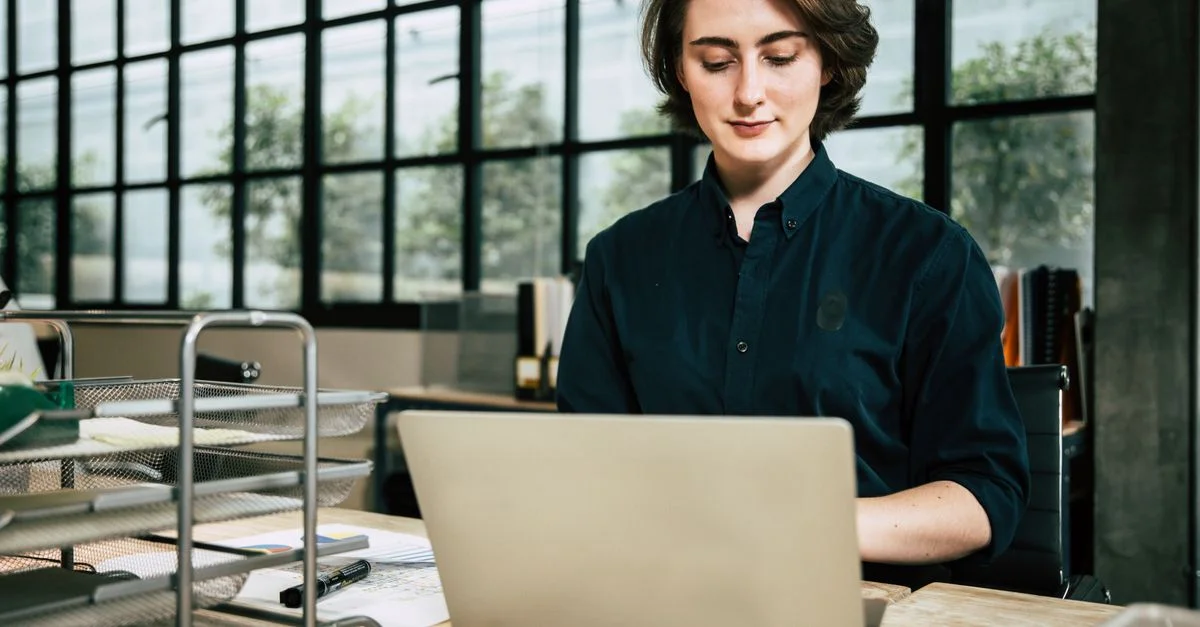 Femme professionnelle utilisant un ordinateur portable dans un environnement de bureau élégant, concentrée sur son travail.