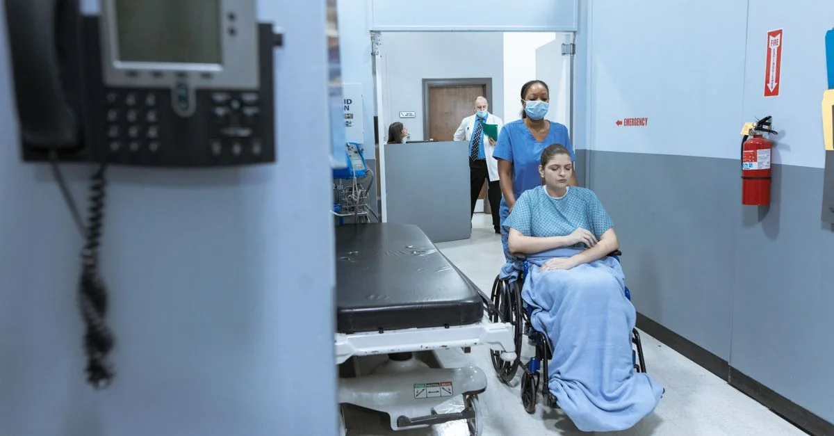 Une infirmière aide un patient en fauteuil roulant dans un couloir d'hôpital, reflétant le soin et le professionnalisme médical.