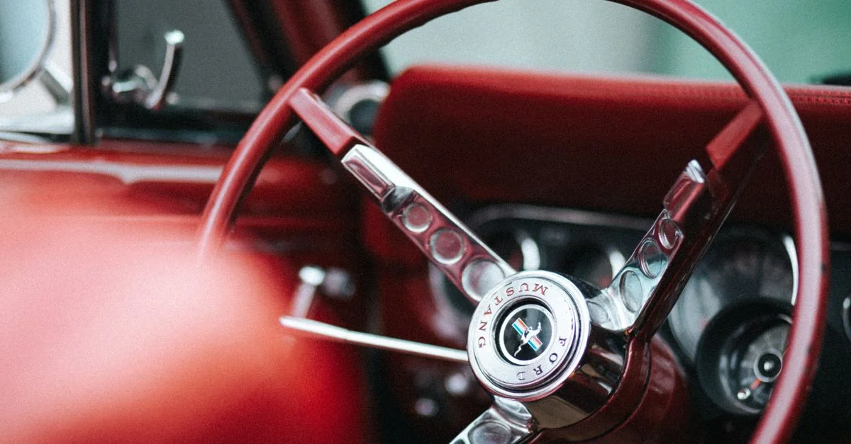 Vue détaillée d'un volant de Ford Mustang vintage avec un intérieur rouge, capturant l'élégance automobile.