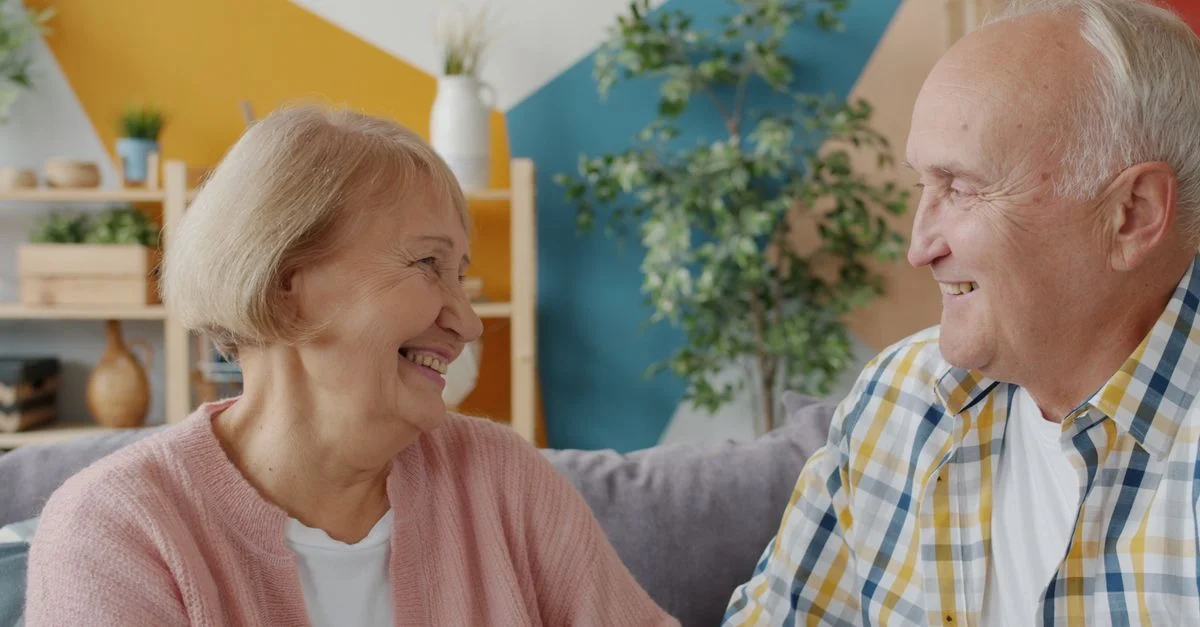 Un couple de seniors heureux partageant un moment de joie à l'intérieur, avec un décor coloré.