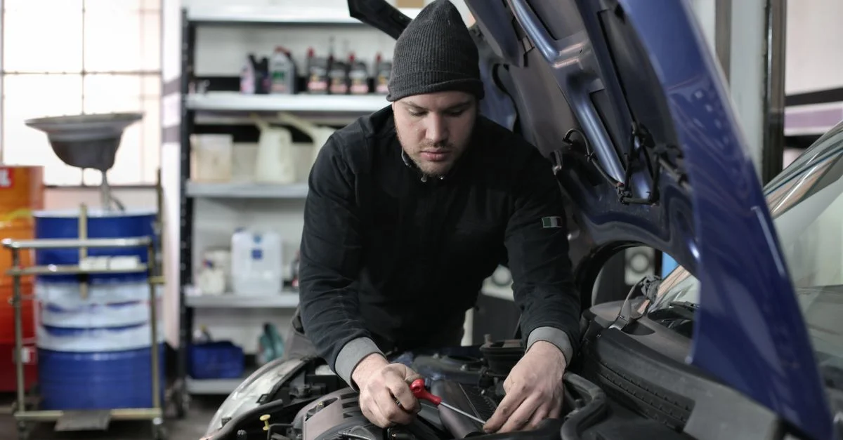 Homme travaillant sous le capot d'une voiture dans un garage, concentré sur la réparation du moteur