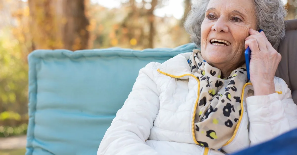 Femme senior souriante parlant sur un téléphone portable en plein air dans un parc, profitant d'un appel joyeux.