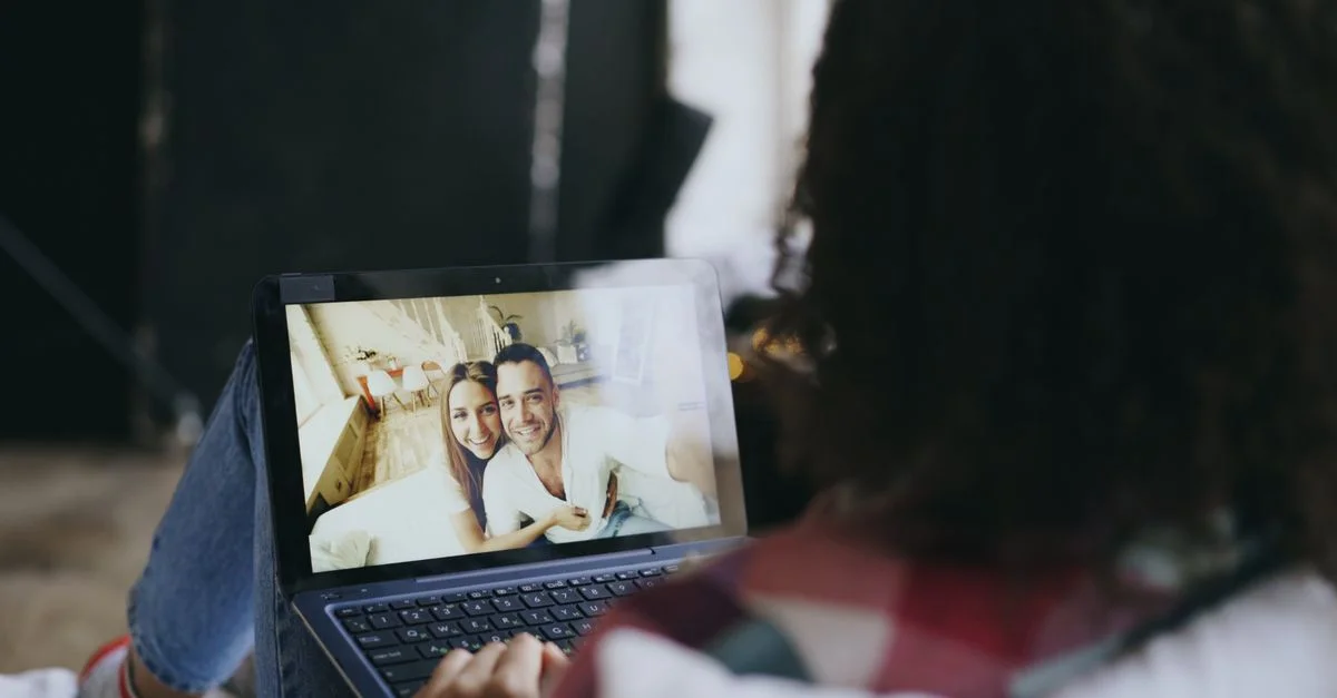 Une femme regarde chez elle la photo d'un couple heureux sur un ordinateur portable, illustrant le lien qui se tisse grâce à la technologie.