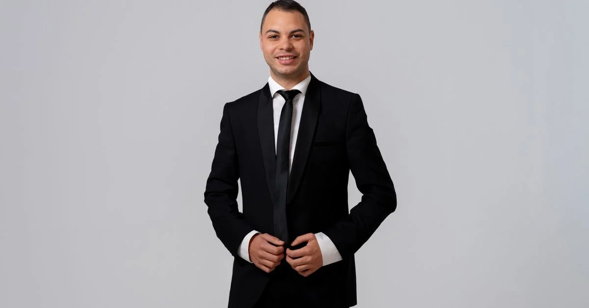 Homme confiant dans un costume noir sur mesure souriant sur fond blanc.