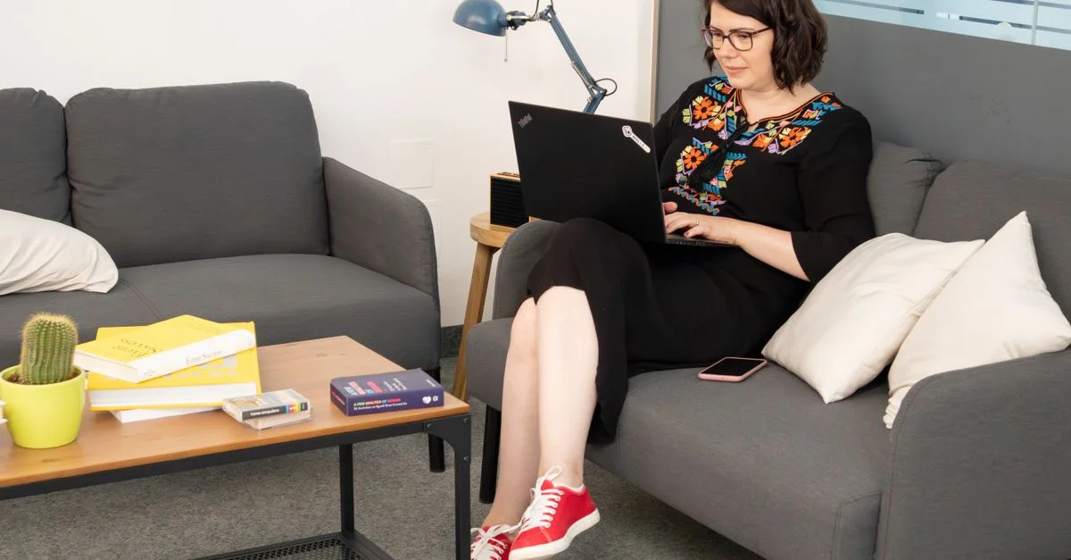 Femme adulte assise sur un canapé utilisant un ordinateur portable dans un cadre de bureau moderne.